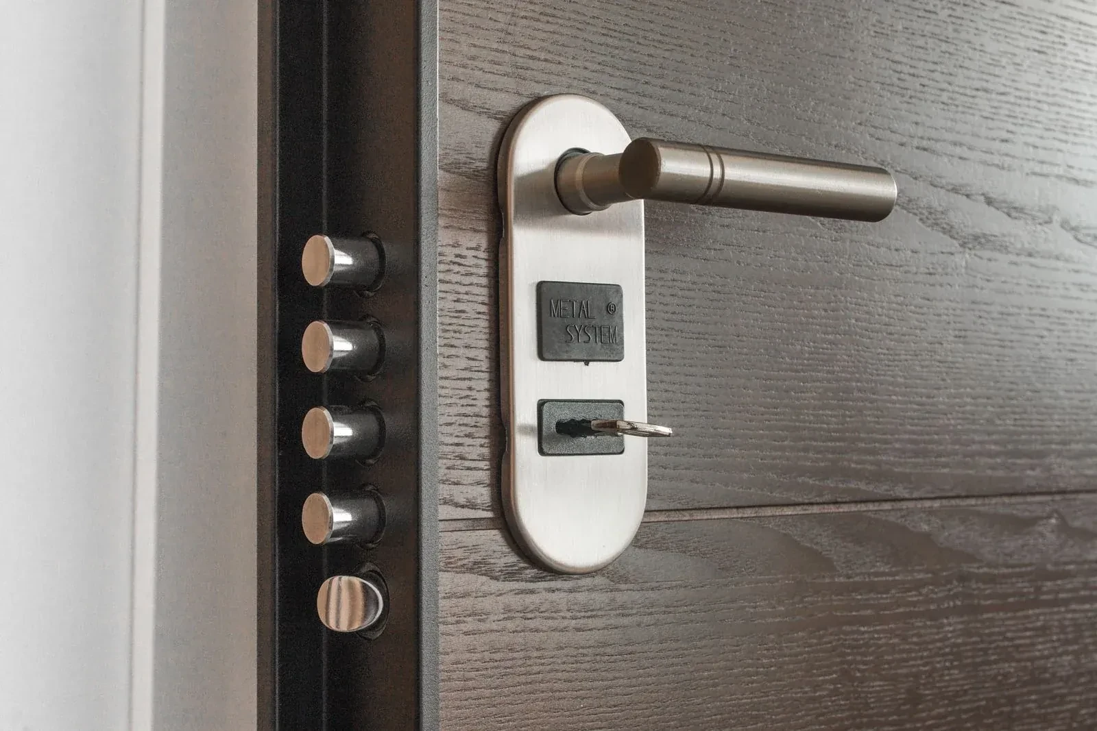 Steel door lever on an oval plate with a key in the lock, beside a row of metal bolts on the edge.